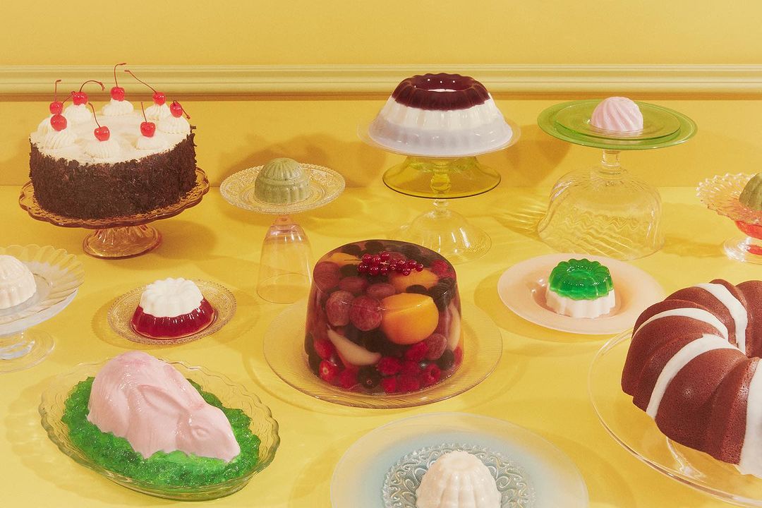 Assortment of colorful gelatin desserts and cakes on glass plates, presented on a yellow table against a matching background.