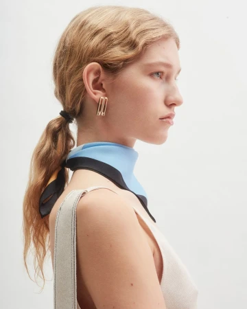 Profile portrait of a woman wearing a blue and black silk scarf and gold earrings against a plain white background