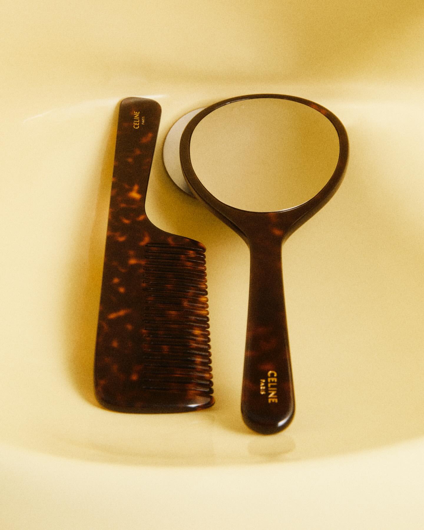 Tortoiseshell-patterned comb and hand mirror set with Celine Paris logo, set against a warm neutral surface, creating a beauty product still life.