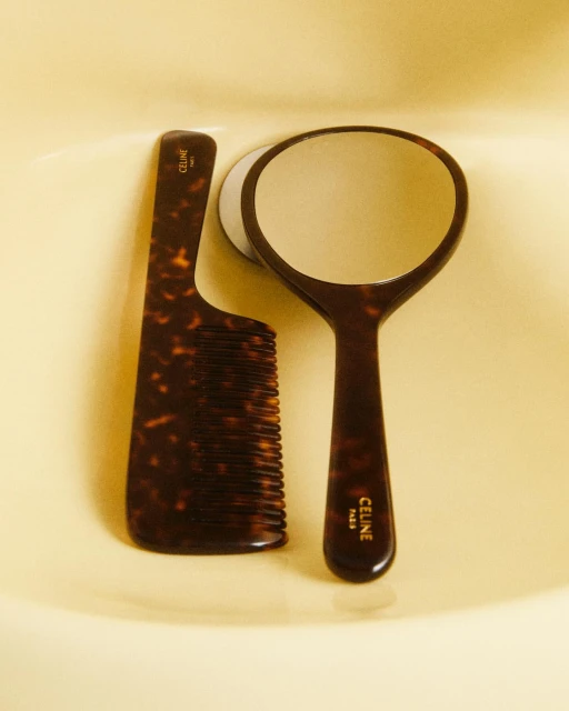 Tortoiseshell-patterned comb and hand mirror set with Celine Paris logo, set against a warm neutral surface, creating a beauty product still life.