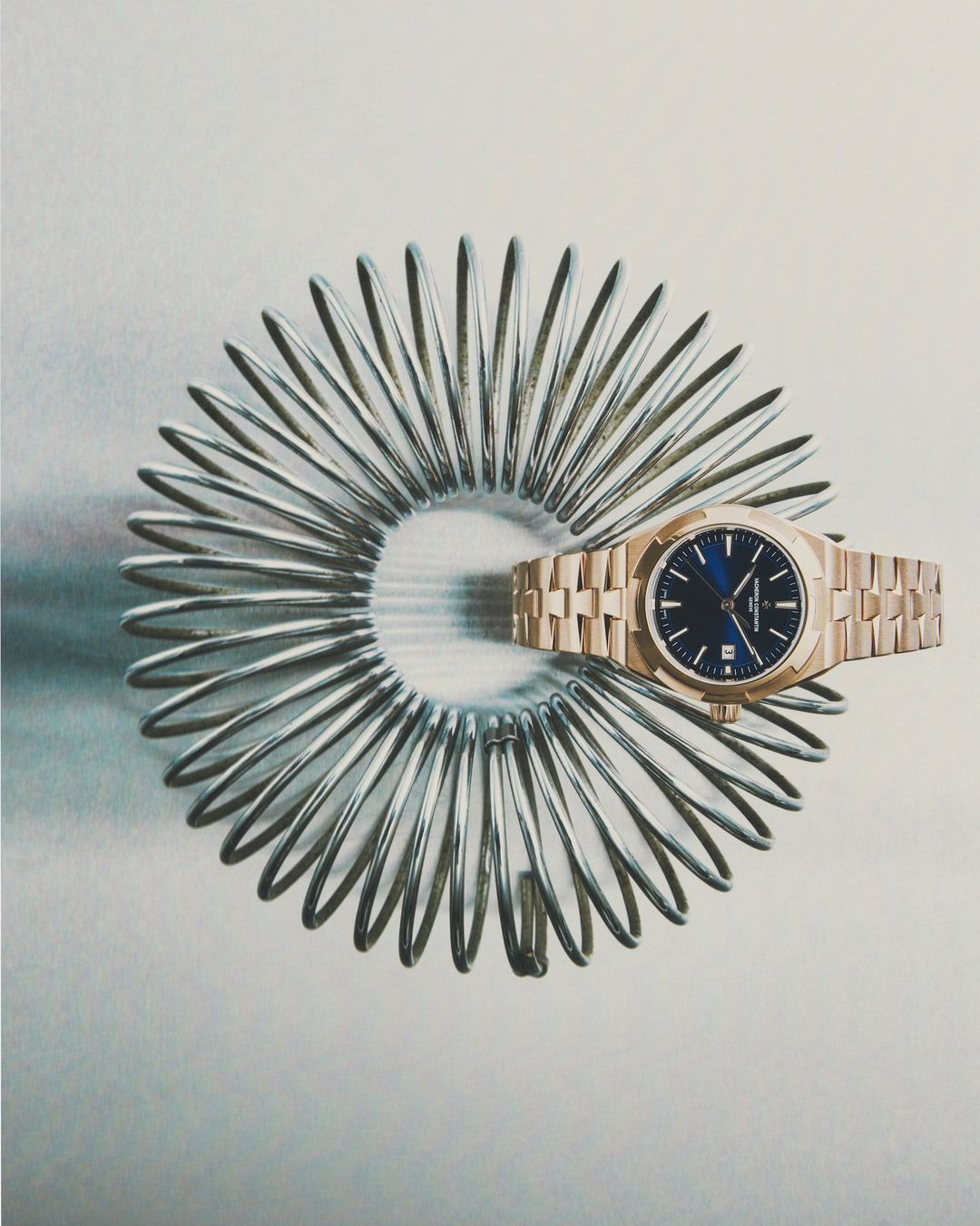A rose gold luxury wristwatch on a stainless steel spring on a light grey background, showcasing elegance, precision, and craftsmanship.