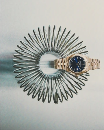 A rose gold luxury wristwatch on a stainless steel spring on a light grey background, showcasing elegance, precision, and craftsmanship.