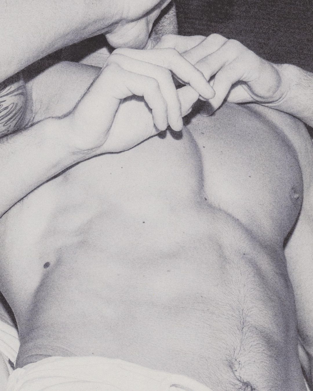 Monochrome close-up of a muscular, shirtless adult male lying down with hands intertwined near his chest in a studio setting.