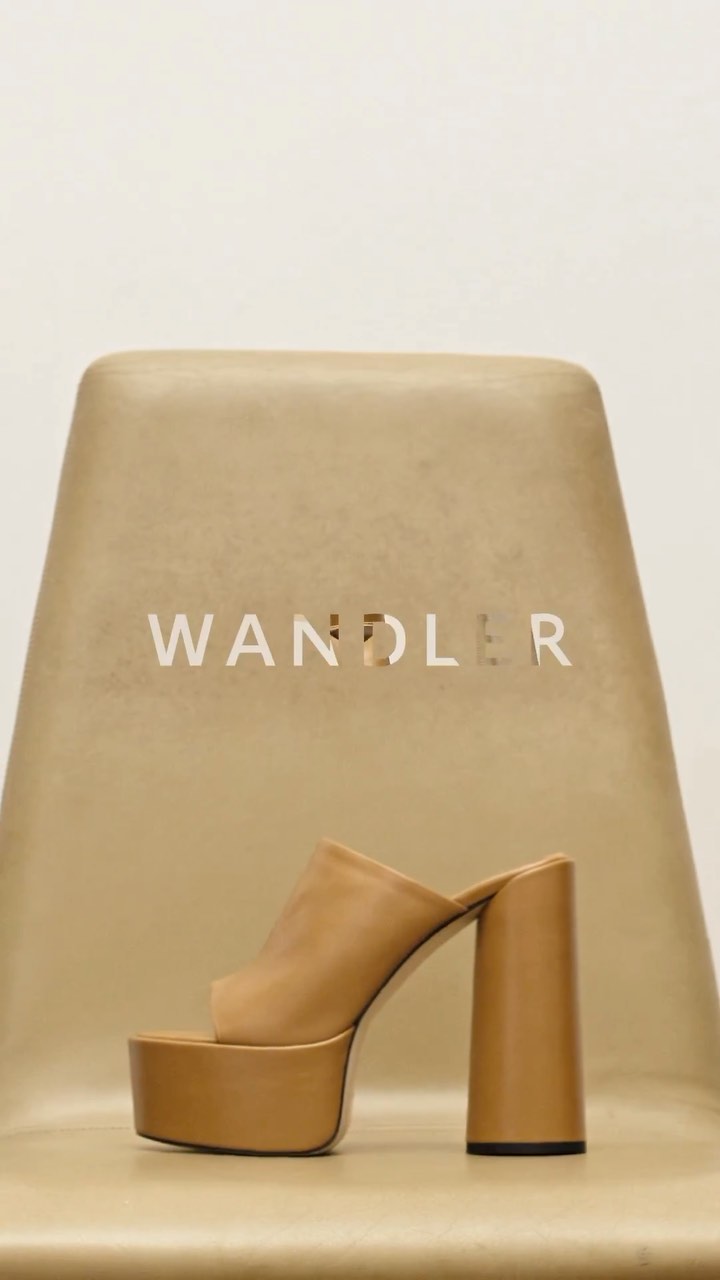 Tan platform mule displayed on a vintage-style chair, product shot, showcasing fashion footwear against neutral background.