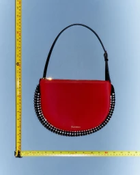 Red leather handbag with crystal embellishments and a black strap against a blue backdrop with measuring tapes