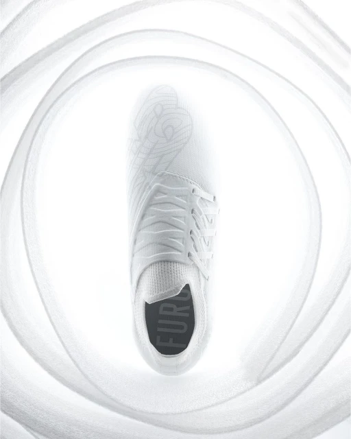A single white sneaker is displayed overhead, surrounded by soft, out-of-focus fabric, creating a bright, minimalist footwear image.