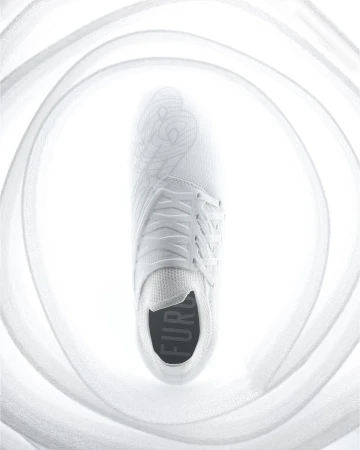 A single white sneaker is displayed overhead, surrounded by soft, out-of-focus fabric, creating a bright, minimalist footwear image.