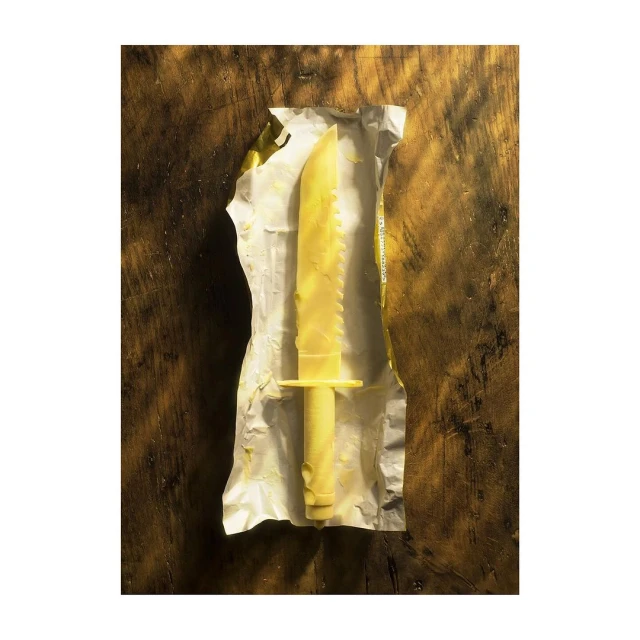 Overhead shot of a butter knife made from butter inside a metallic wrapper on top of a dark brown wooden surface.