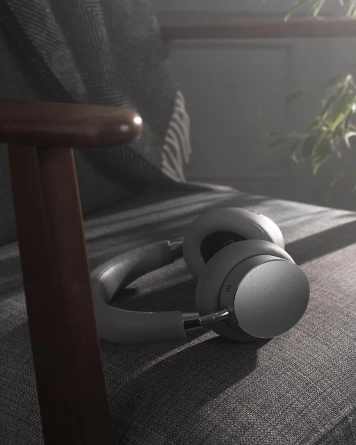 Beige wireless headphones rest on a gray armchair, bathed in diffused daylight filtering through nearby indoor plants.
