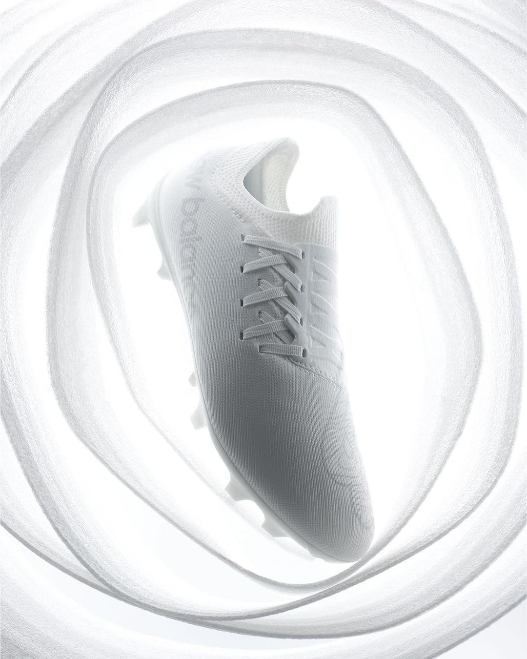 Studio shot of a single white New Balance soccer shoe floating in front of layered white fabric creating a bright, minimalist product image.
