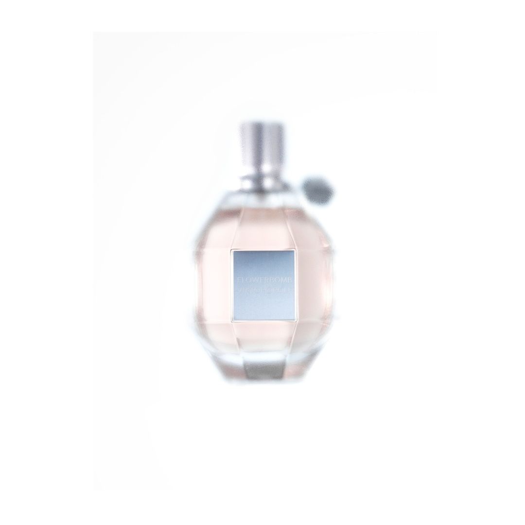 Still life shot of a rounded faceted glass perfume bottle with silver accents and a light pink liquid inside against a white backdrop.