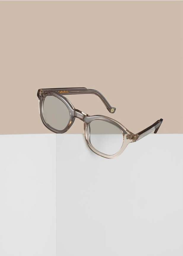 Studio product shot of gray cat-eye eyeglasses resting on a white surface against a neutral background. Fashion eyewear and neutral tones.