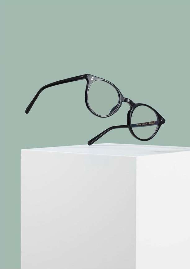 Black eyeglasses on a white cubic surface against a light green background, showcasing eyewear product photography.