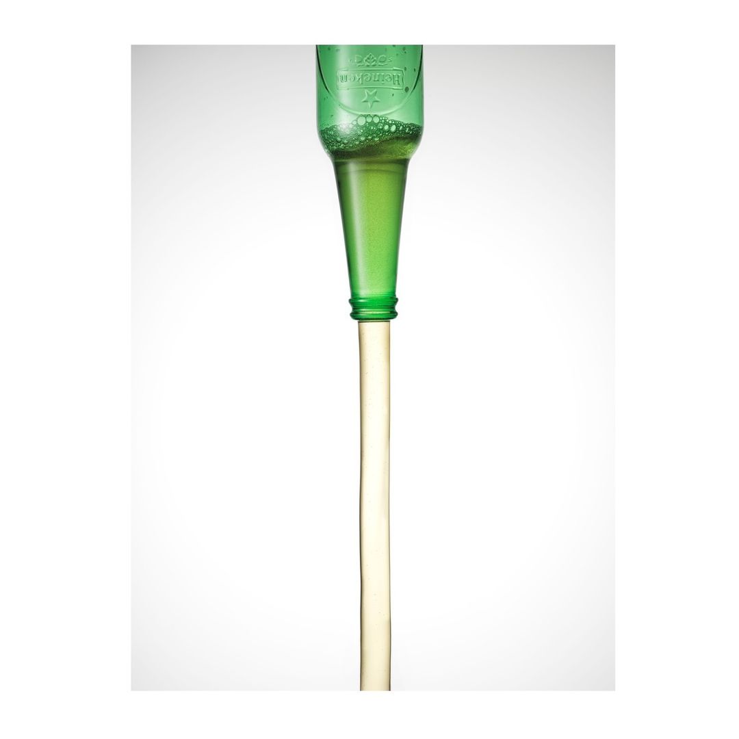 Close-up shot of a green bottle pouring clear liquid, creating a visually striking composition against a bright white background.