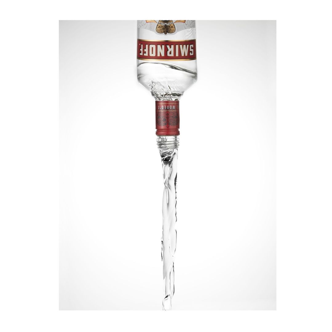 Upside-down Smirnoff vodka bottle with liquid pouring out in a high-key white studio shot with a focus on branding and fluid dynamics.