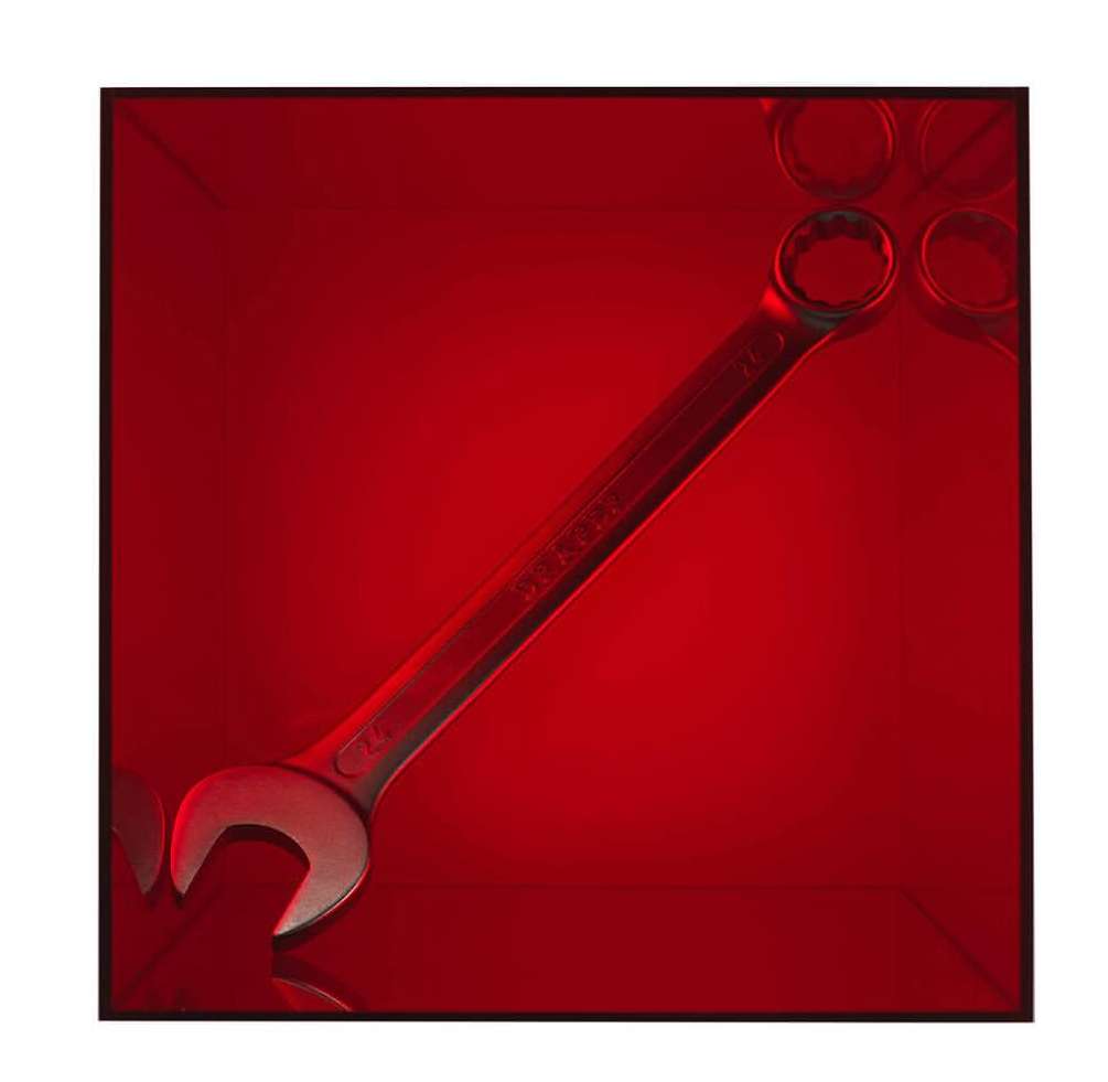 Close-up studio shot of a silver-tone combination wrench with box end and open end against a graduated red backdrop with tool outlines.