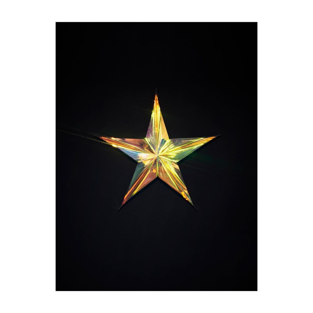 Iridescent star-shaped decoration on a black backdrop, featuring a reflective surface with hues of gold, green, and purple.