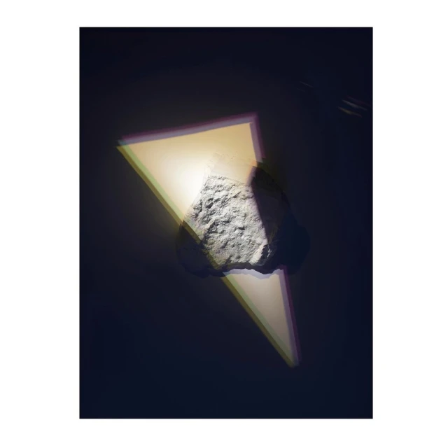 Abstract studio shot of a textured rock with a triangular light projection against a dark backdrop creating a surreal and modern aesthetic.