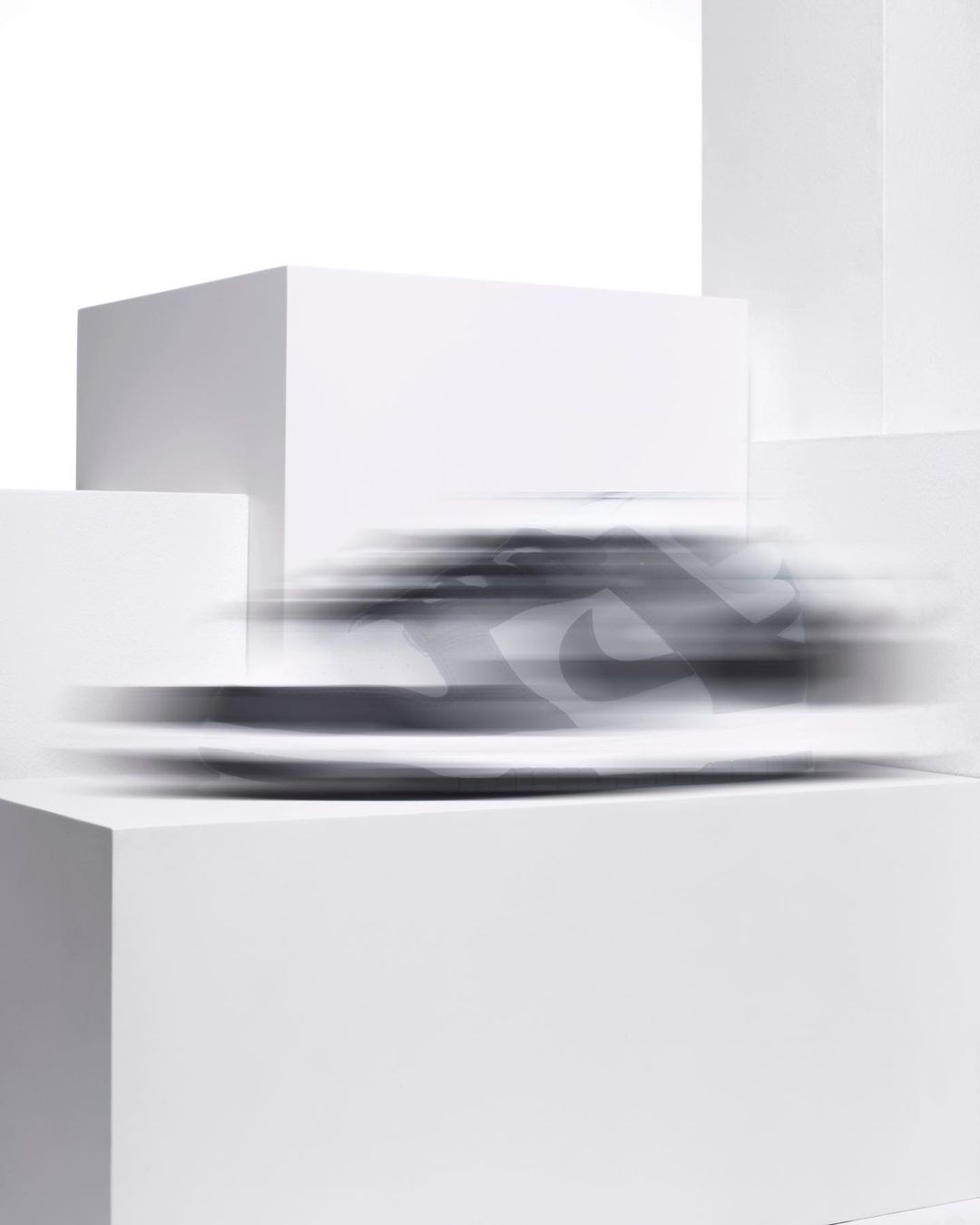 Dynamic studio shot of a blurred athletic shoe with a white background, placed on a stepped white cube platform, promoting motion and speed.