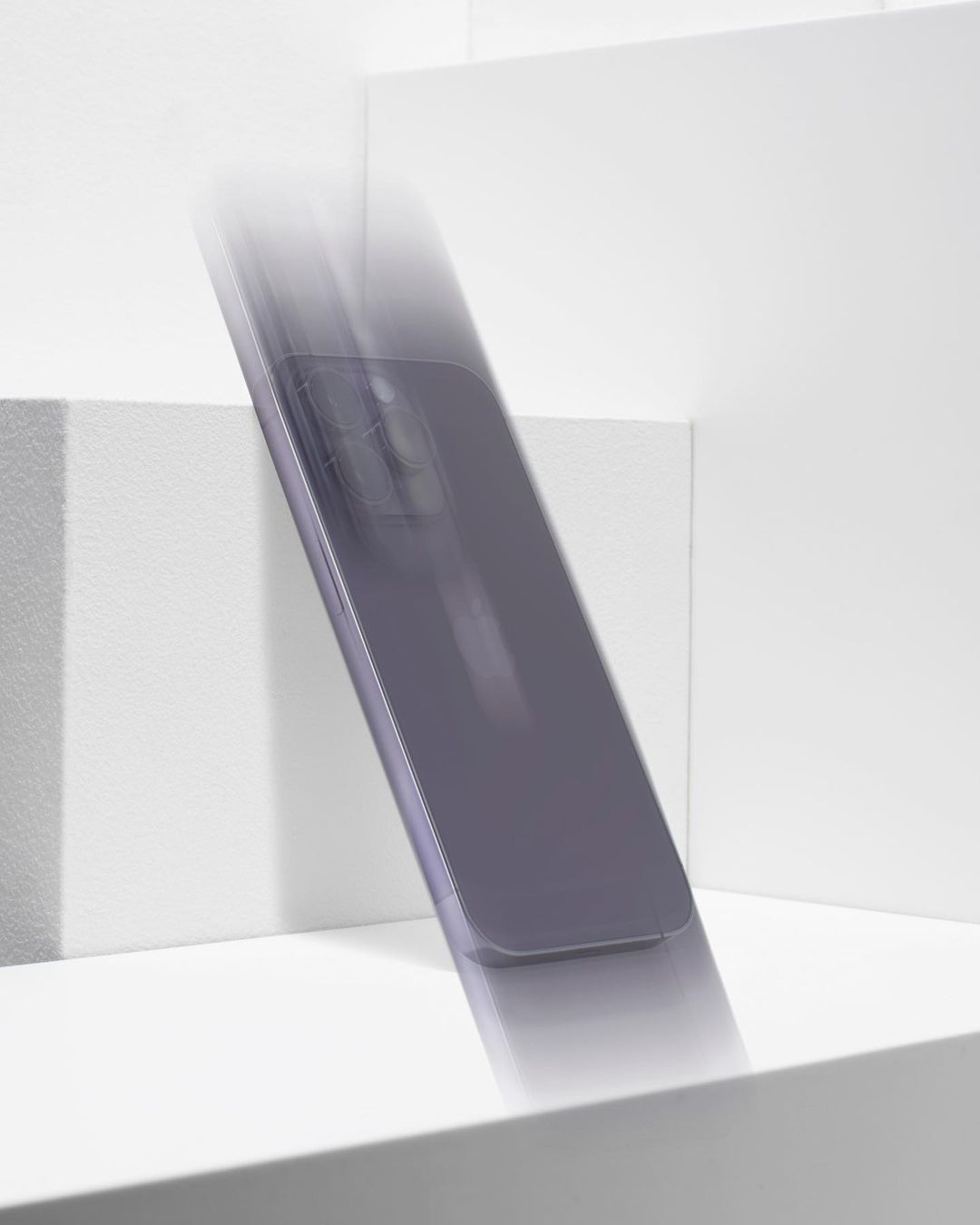 Product photography of a gray smartphone in motion on a bright white geometric surface, with blurred movement emphasizing its design.