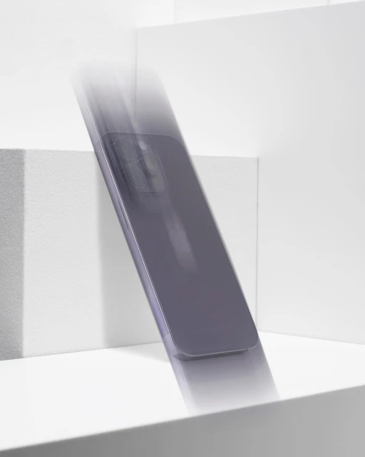 Product photography of a gray smartphone in motion on a bright white geometric surface, with blurred movement emphasizing its design.