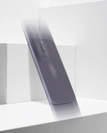 Product photography of a gray smartphone in motion on a bright white geometric surface, with blurred movement emphasizing its design.
