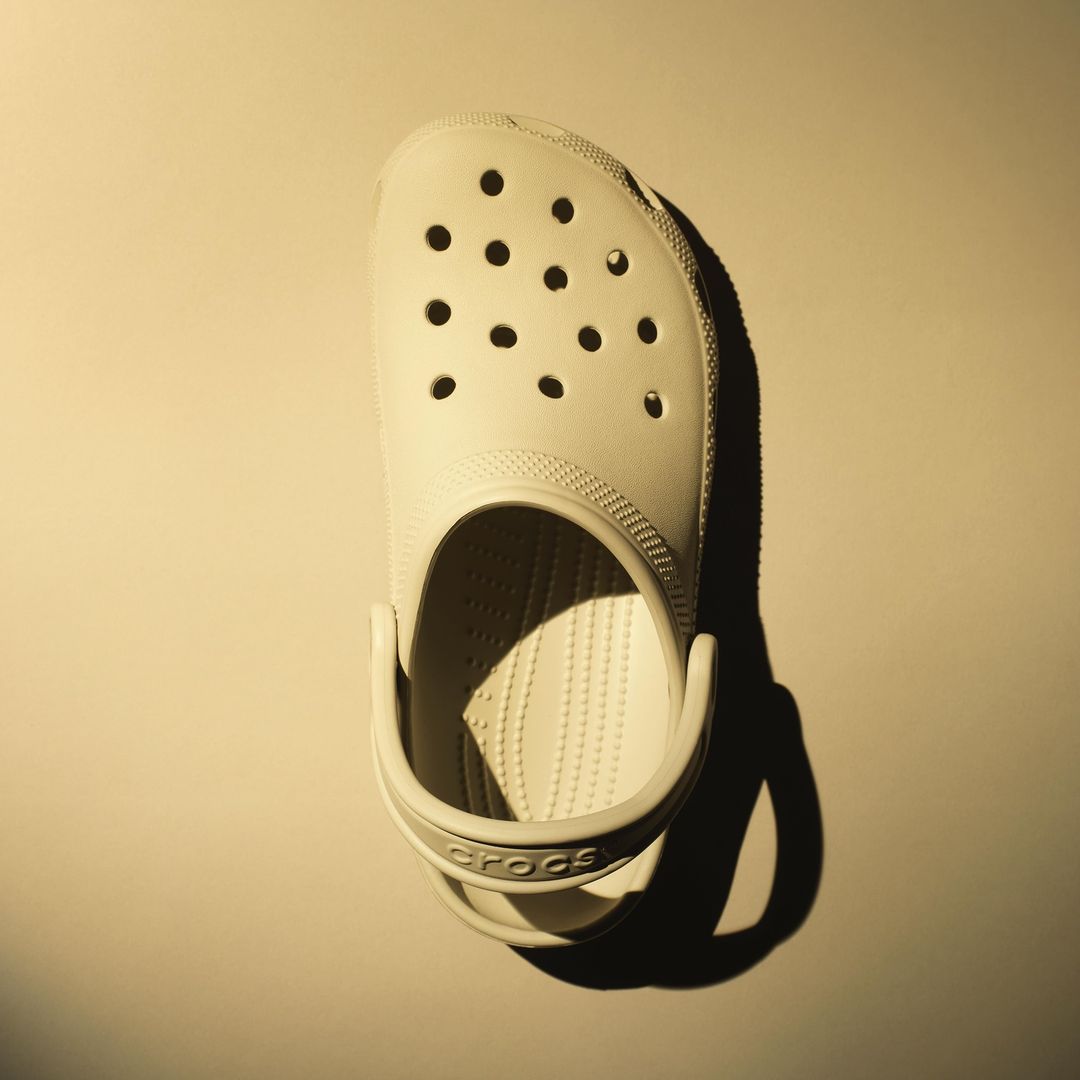 Single light yellow Croc shoe isolated on a solid light yellow background, showcasing the brand logo and distinctive design.