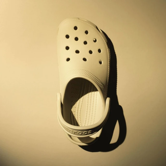 Single light yellow Croc shoe isolated on a solid light yellow background, showcasing the brand logo and distinctive design.