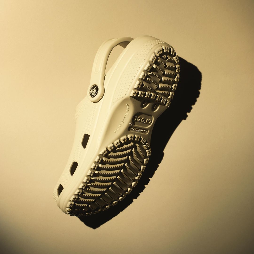 Angled product shot of a single, off-white Croc showcasing its sole and design details against a neutral backdrop with diffused lighting.