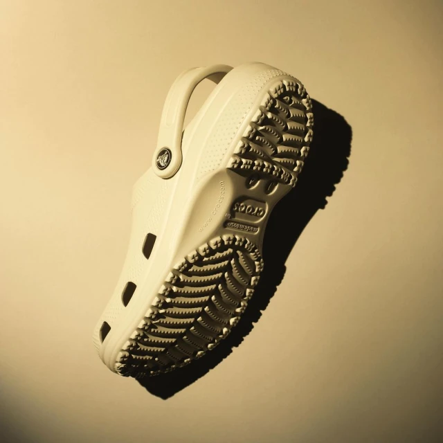 Angled product shot of a single, off-white Croc showcasing its sole and design details against a neutral backdrop with diffused lighting.