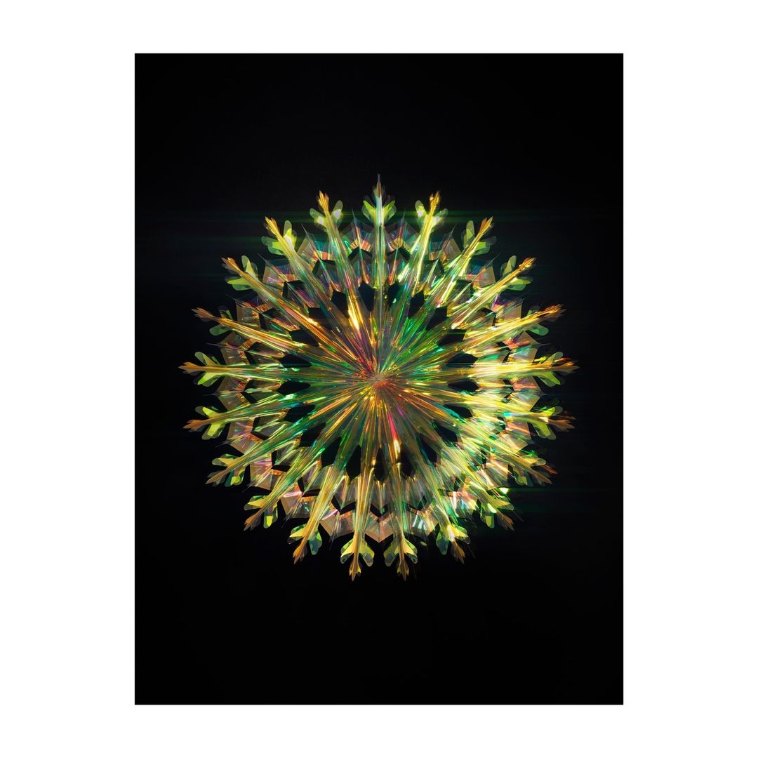 Close-up of a multi-colored snowflake decoration with a radial design isolated against a dark black background in a studio setting.