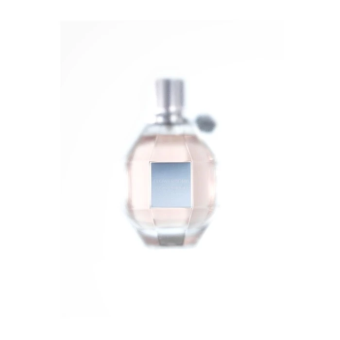 Close-up product photograph of a faceted glass perfume bottle with pale liquid on a white background by Rowan Fee.