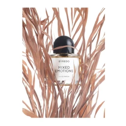 Byredo Mixed Emotions perfume bottle surrounded by dry brown leaves against a white background