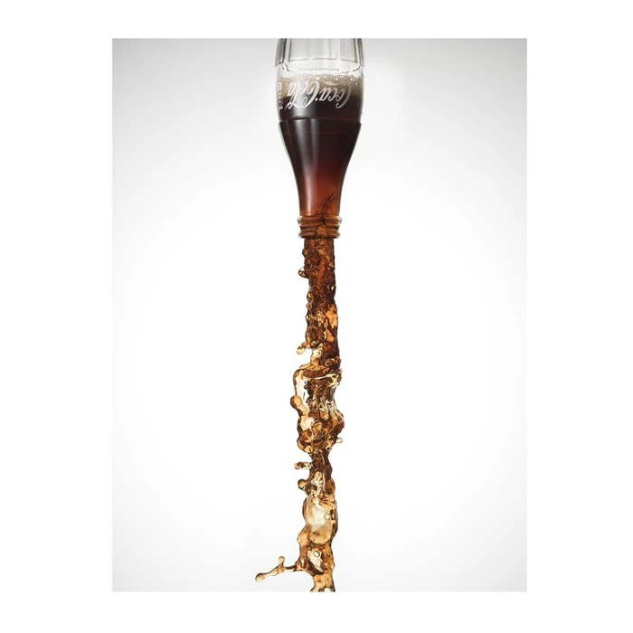 Upside down Coca-Cola bottle pouring a dynamic dark carbonated liquid stream against a white background