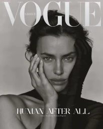 Close-up portrait of Irina Shayk with dark hair and black gloves touching her face against a neutral studio background