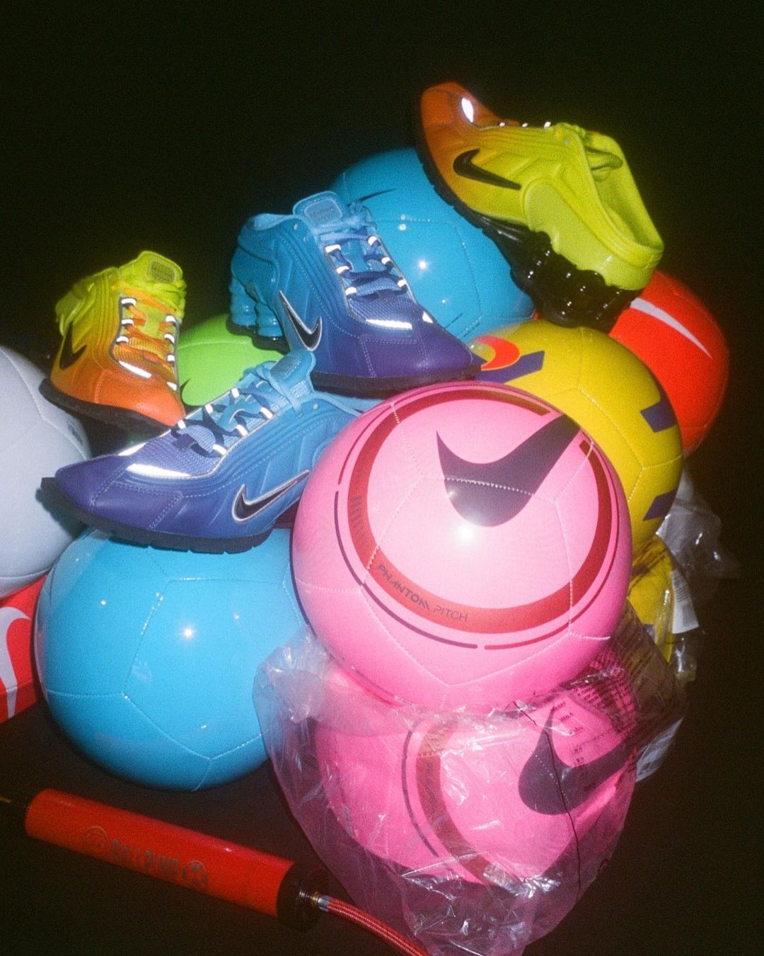 Pile of colorful Nike soccer balls and athletic shoes, close-up product shot, studio setting, showcasing sports equipment and footwear.