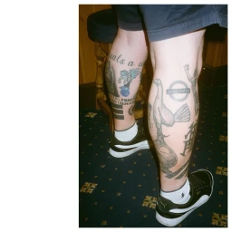 Close-up portrait of heavily tattooed legs wearing black sneakers and white socks against a patterned carpet in London.