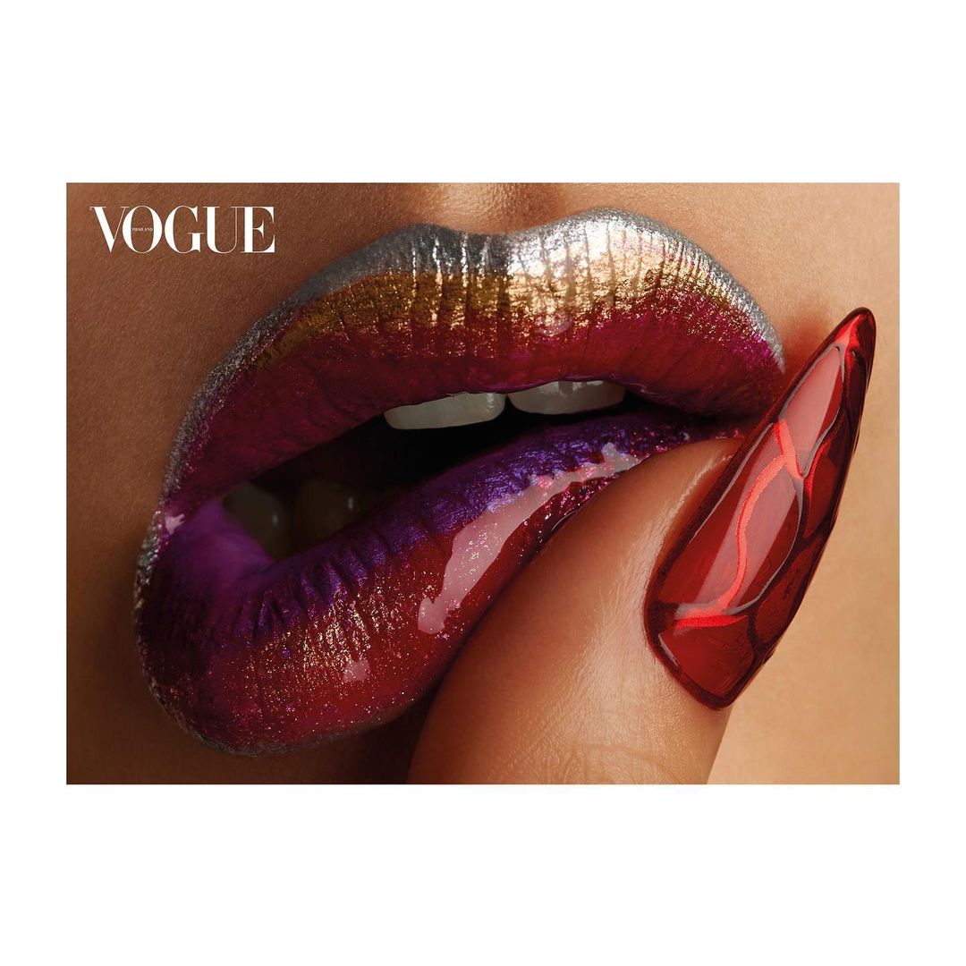 Close-up of metallic makeup on a woman's lips, red fingernail with abstract detail; beauty shot with a fashion magazine logo.