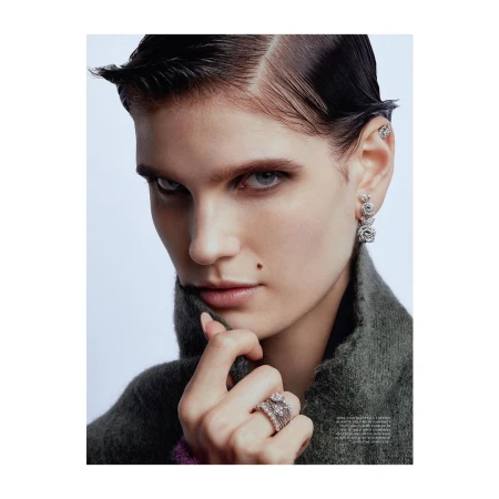 Close-up portrait of a woman wearing diamond rose earrings and stacked rings with a dark turtleneck.