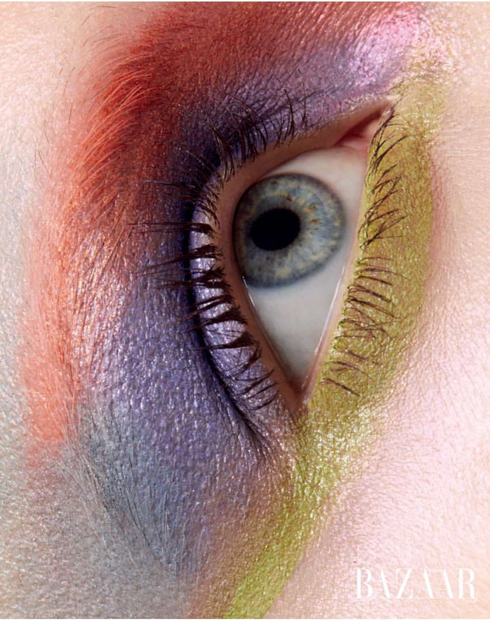 Close-up of a blue eye surrounded by orange, purple, and yellow eyeshadow with 'BAZAAR' logo at the bottom of the frame.