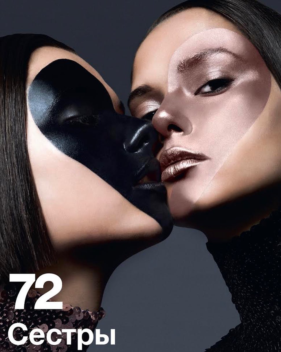 Two women with artistic face makeup in a close-up shot, embracing; one face has bronze tone while the other has black face paint.