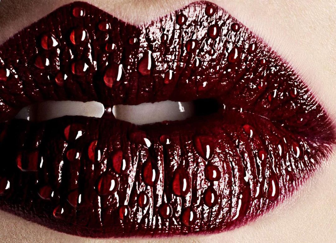 Macro close-up of a woman's red lips covered in water droplets, highlighting beauty and makeup artistry in a studio setting.