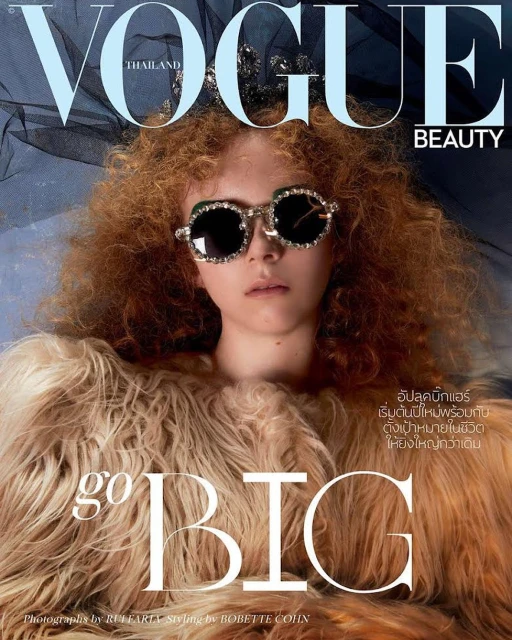 Vogue Thailand cover featuring a woman with curly red hair, bejeweled sunglasses, and a fur coat, against a blue backdrop with Vogue branding.