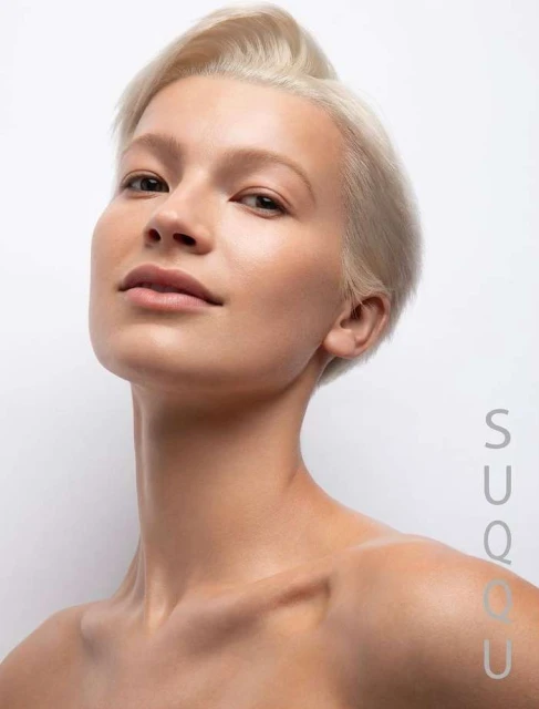 Close-up portrait of a fair-skinned woman with short blonde hair looking upwards against a plain white backdrop, skincare beauty.