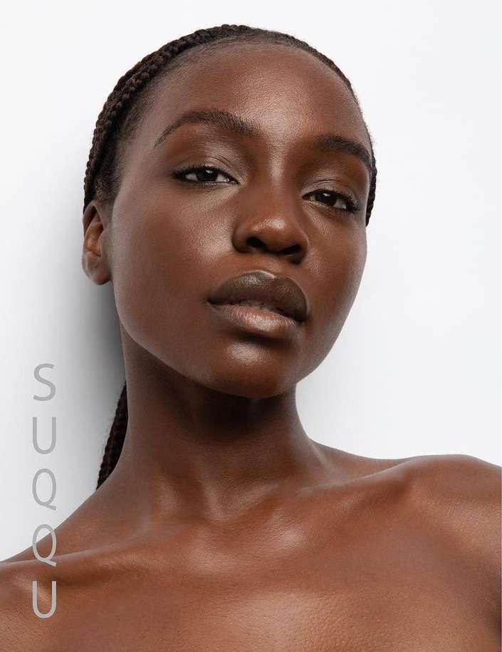 Close-up portrait of a single adult female with dark skin and braided hair against a bright background, emphasizing beauty and skincare.