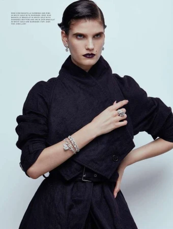 Model wearing dark coat and diamond jewelry against a pale background, photographed by Rui Faria