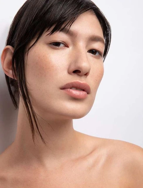 Portrait of an Asian woman with a neutral expression against a white backdrop, showcasing a natural and minimalist beauty aesthetic.