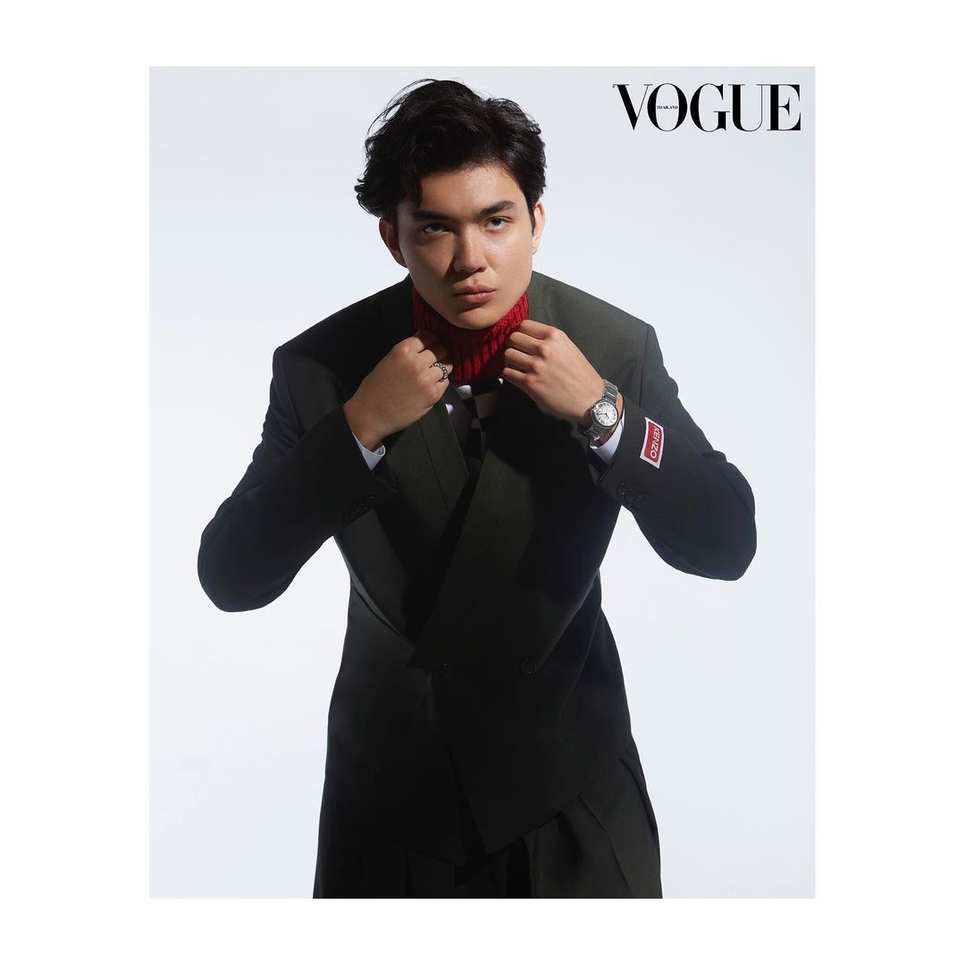Portrait of a young Asian man in a black suit and red turtleneck posing against a white backdrop for a fashion editorial in Vogue.