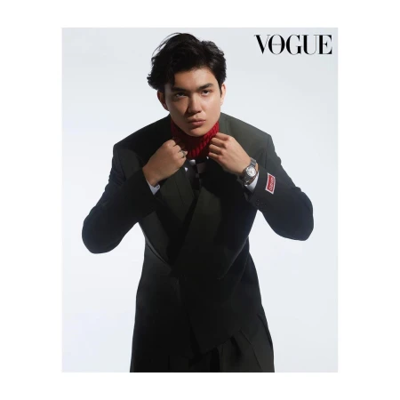 Portrait of a young Asian man in a black suit and red turtleneck posing against a white backdrop for a fashion editorial in Vogue.