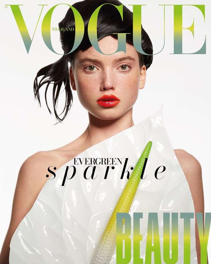 Vogue Thailand cover featuring a woman with black hair and orange lips, adorned with a white anthurium flower and wearing a glossy plastic wrap.